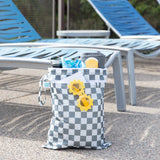Bumkins Wet/Dry Bag: Charcoal Check holds sunglasses, a water bottle, and swim essentials next to two empty lounge chairs.