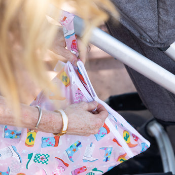 A person unzips a Bumkins Wet/Dry Bag: Boots attached to a stroller handle.