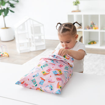 A child opens a Bumkins Wet Bag + Wet/Dry Bag Set: Boots, featuring colorful prints, at a white table in a bright room.