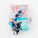 A towel, sunglasses, book, water bottle, and swimwear peek out from Bumkins Wet/Dry Bag: Boots on a white background.