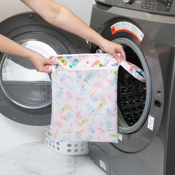 A person holds a bag from Bumkins Wet Bag + Wet/Dry Bag Set: Boots in front of an open front-loading washing machine.