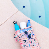 Bumkins Wet/Dry Bag: Yoga Pals rests on a pool deck with a water bottle, towel, sunscreen, magazine, and sunglasses peeking out.