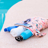 Bumkins Wet/Dry Bag: Yoga Pals lays next to a pool with a towel, sunglasses, magazine, water bottle, and sunscreen inside.