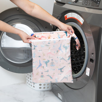 A person holds a Bumkins Wet/Dry Bag: Yoga Pals in front of a front-loading washing machine.