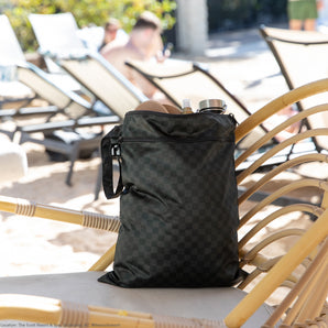 Roamio by Bumkins Wet/Dry Bag: Rich Black holds shoes and a water bottle on a rattan chair with lounge chairs in the background.