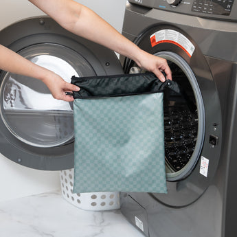 A person holds Bumkins Wet/Dry Bag: Rich Black in front of a front-loading washing machine.