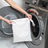 A person holds a Bumkins Wet/Dry Bag: Wander in front of an open front-loading washing machine.