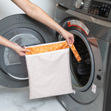 A person holds a bag from Bumkins Wet Bag + Wet/Dry Bag Set: Grounded in front of an open front-loading washing machine.