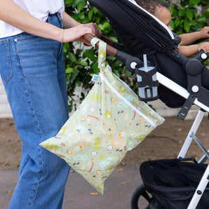 A parent hangs the Bumkins Wet Bag + Wet/Dry Bag Set: Camp Gear from a stroller while enjoying nature with their baby.