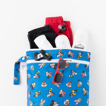 Bumkins Wet/Dry Bag: Mickey & Friends Forever holds red and black clothes, white shoes, and red sunglasses on a white background.