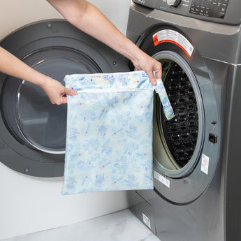 A person holds a bag from Bumkins Wet Bag + Wet/Dry Bag Set: Aloha Stitch in front of an open front-loading washing machine.