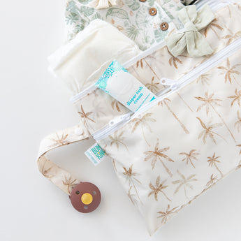 Close-up of a bag from Bumkins The Chaos Coordinator Deluxe 5-Piece Set: Palm Daze with baby clothes and essentials on a white background.