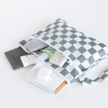 Bumkins Wet Bag + Wet/Dry Clutch + Clear Travel Bag 3 Pack in Charcoal Check shown with travel essentials on a white surface.