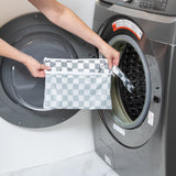 A person holds a bag from Bumkins The Chaos Coordinator Deluxe 5-Piece Set: Charcoal Check in front of an open front-loading washing machine.