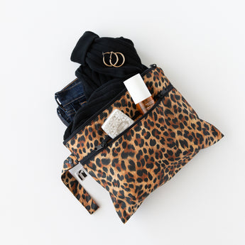 A bag from Roamio by Bumkins Wet Bag + Wet/Dry Clutch Set: Leopard holds clothes and toiletries on a white background.