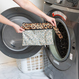 A person holds Roamio by Bumkins Wet/Dry Clutch: Leopard in front of an open front-loading washing machine.