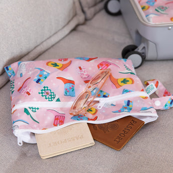 Passports spill out of a bag from Bumkins Wet Bag + Wet/Dry Clutch Set: Boots on a couch with sunglasses and a suitcase nearby.