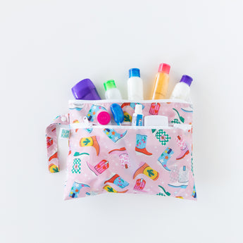A bag from Bumkins On-The-Go Mealtime 6-Piece Set: Boots + Pink holds travel-size toiletries on a white background.