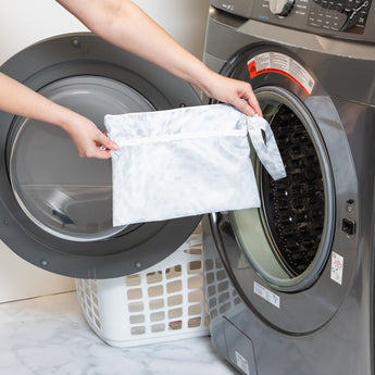 A person holds Roamio by Bumkins Wet/Dry Clutch: Disco Check in front of an open front-loading washing machine.