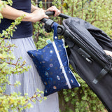A close-up of a Bumkins Wet/Dry Clutch: Evil Eye attached to a stroller against lush greenery in the background.