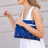 A person in white holds a Bumkins Wet/Dry Clutch: Evil Eye with mystical symbols, made of waterproof fabric.