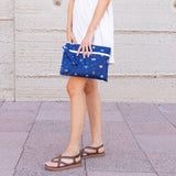 Someone in a light dress holds a Bumkins Wet/Dry Clutch: Evil Eye on tiled pavement against a plain wall.