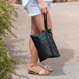 A woman in shorts and sandals holds a bag from Roamio by Bumkins Wet Bag + Wet/Dry Clutch Set: Rich Black outdoors by greenery.