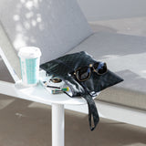 Roamio by Bumkins Wet/Dry Clutch: Rich Black sits on a table outdoors next to a lounge chair with sunglasses, books, and a coffee cup.