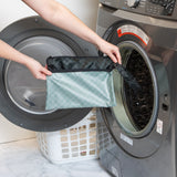 A person holds a bag from Roamio by Bumkins Wet Bag + Wet/Dry Clutch Set: Rich Black in front of an open front-loading washing machine.