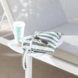 Roamio by Bumkins Wet/Dry Clutch: Clubhouse Stripe with sunglasses & a coffee cup sits on a table in sunlight next to a gray cushioned chair.