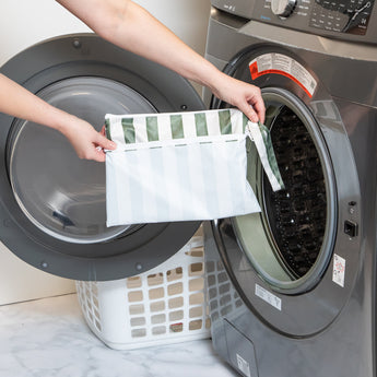 A person holds Roamio by Bumkins Wet/Dry Clutch: Clubhouse Stripe in front of an open front-loading washing machine.