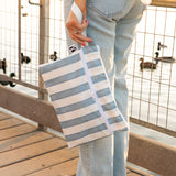 A person in light jeans holds a Roamio by Bumkins Wet/Dry Clutch: Nautical Stripe  by a lakeside fence with ducks in background.