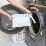 A person holds Roamio by Bumkins Wet/Dry Clutch: Nautical Stripe in front of an open front-loading washing machine.