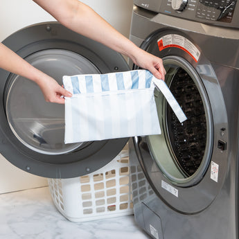A person holds Roamio by Bumkins Wet/Dry Clutch: Nautical Stripe in front of an open front-loading washing machine.