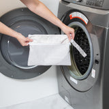 A person holds a bag from Bumkins The Chaos Coordinator Deluxe 5-Piece Set: Wander in front of an open front-loading washing machine.