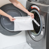A person holds a bag from Bumkins Wet Bag + Wet/Dry Clutch Set: Wander in front of an open front-loading washing machine.