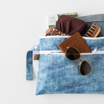 A bag from Roamio by Bumkins The Commuter Deluxe 5-Piece Set: Denim On Denim with vacation essentials on a white background.