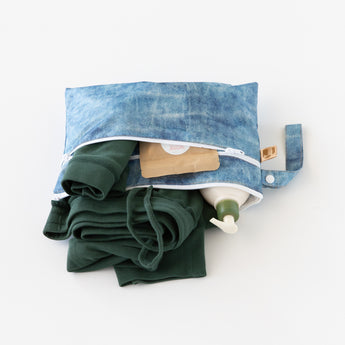 Roamio by Bumkins Wet/Dry Clutch: Crushed Denim lays open on a white background, holding clothes, a lotion bottle, and brown packet.