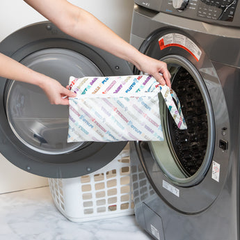 A person holds Bumkins Wet/Dry Clutch: Mickey & Friends Varsity in front of an open front-loading washing machine.