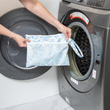 A person holds a bag from Bumkins The Chaos Coordinator Deluxe 5-Piece Set: Disney Aloha Stitch in front of an open washing machine.