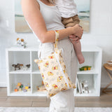 A woman holds a baby & a bag from Bumkins The Chaos Coordinator Deluxe 5-Piece Set: Disney Pooh Bear + Friends in front of toys on shelves.
