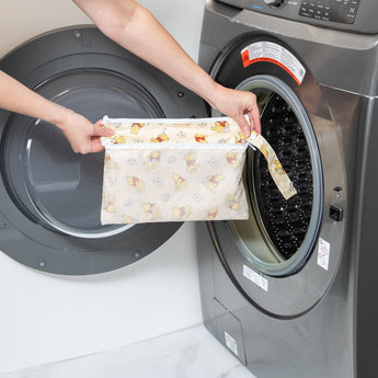 A person holds a Bumkins Wet/Dry Clutch: Winnie Loves Hunny in front of a front-loading washing machine.