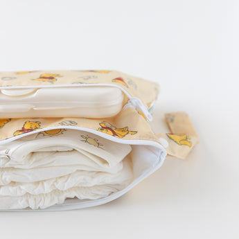 Close-up of Bumkins Wet/Dry Clutch: Winnie Loves Hunny holding diapers, wipes, and clothes on a white background.