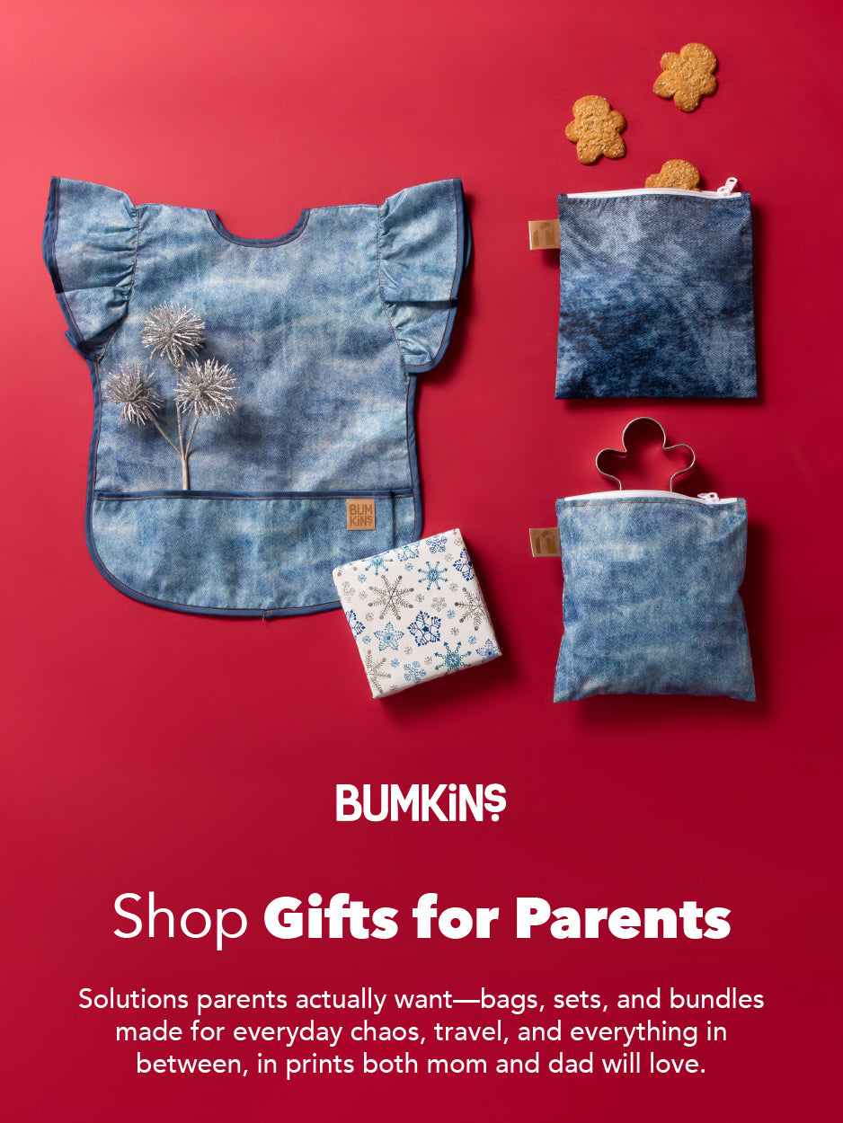 Blue baby bib, printed pouches, and a gift box on a red background with cookies, promoting Bumkins gifts for parents.
