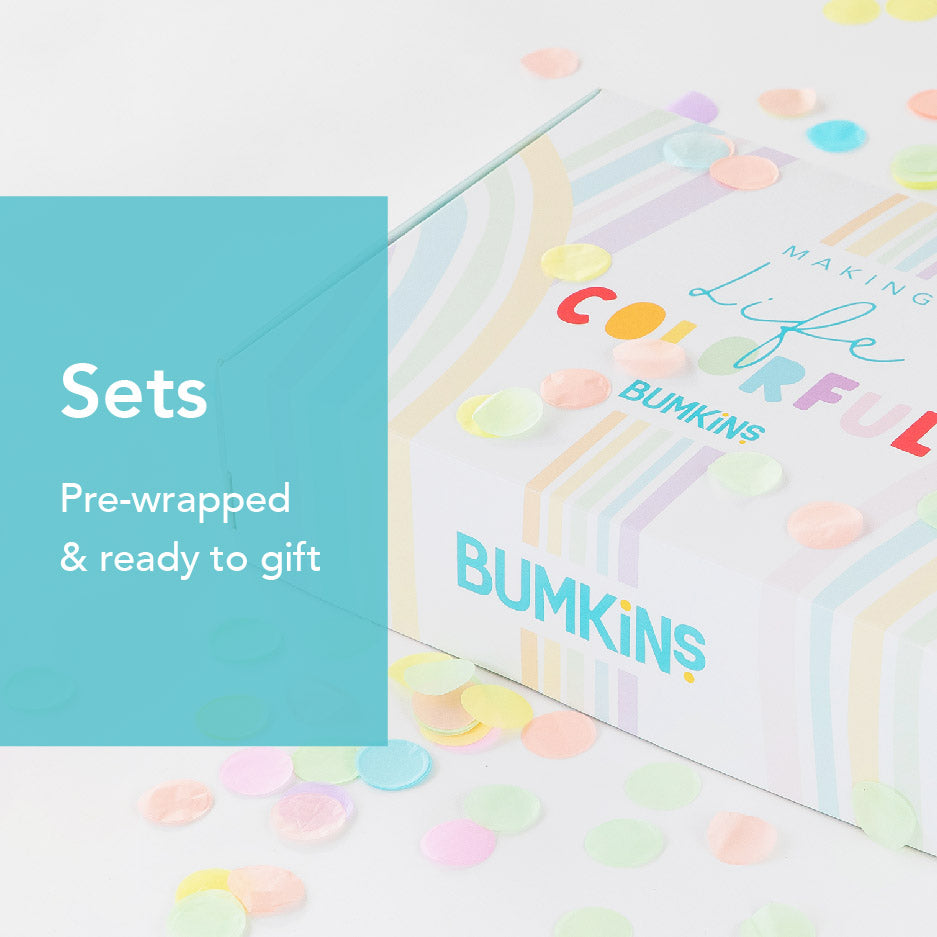 A decorative gift box with pastel rainbow stripes and the text BUMKINS and Making Life Colorful. The background is sprinkled with colorful confetti. A teal overlay reads Sets Pre-wrapped & ready to gift.