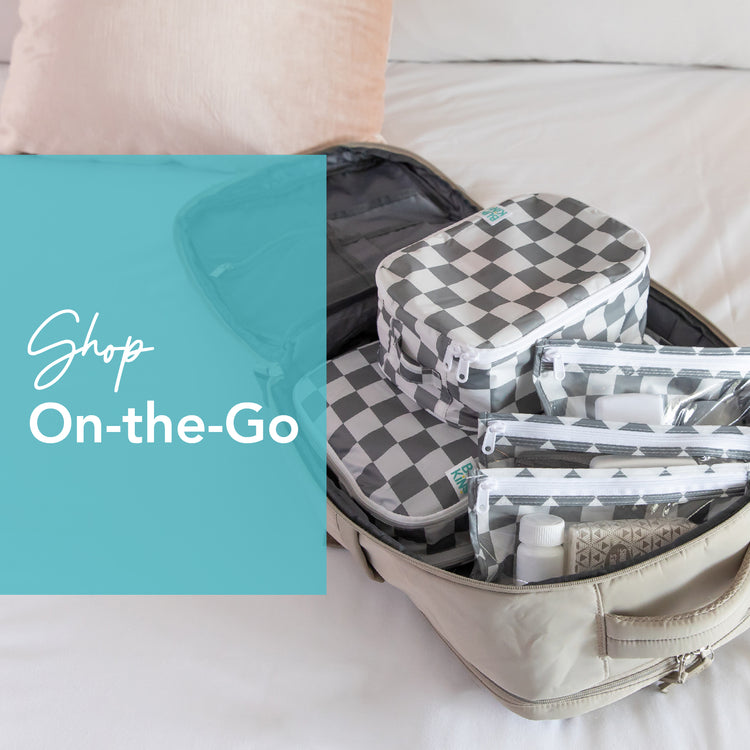 An open suitcase on a bed is neatly packed with checkered travel bags and clear pouches containing toiletries. A pink pillow is in the background. Text on the image reads, Shop On-the-Go.