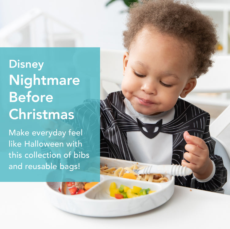 A toddler wearing a black and white outfit is eating from a divided plate with pasta and fruit. A text overlay on the left reads: Disney Nightmare Before Christmas. Make everyday feel like Halloween with this collection of bibs and reusable bags!.