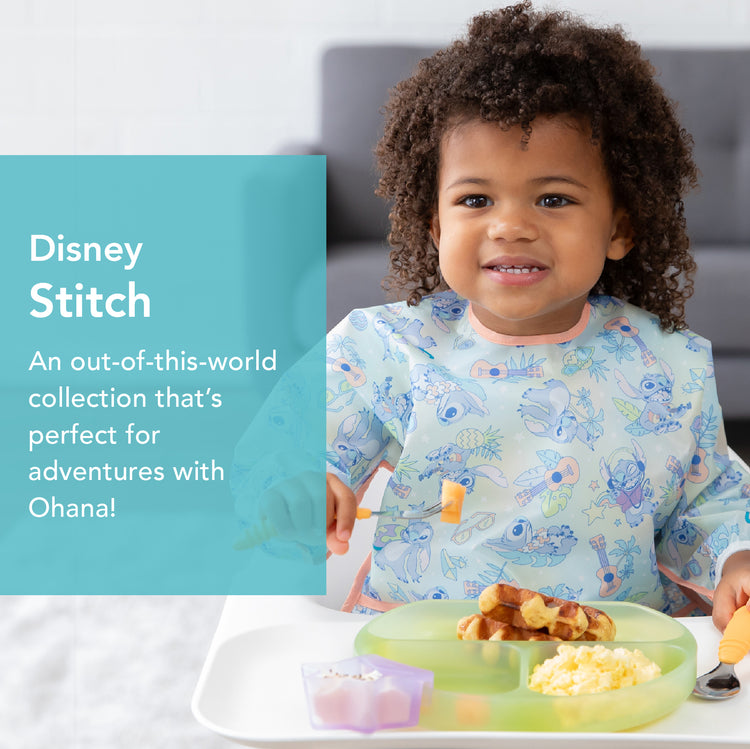 A toddler sitting at a table wearing a bib with Disney Stitch designs, eating waffles and scrambled eggs from a green plate. A small cup of fruit is in front of them. Theres text on the left side with Disney Stitch branding.