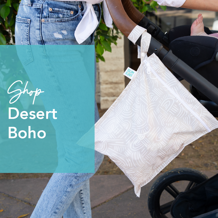 A person pushing a stroller adorned with a patterned white bag labeled Planet Wise. A blue overlay reads Shop Desert Boho. Denim clothing and a glimpse of greenery are visible.