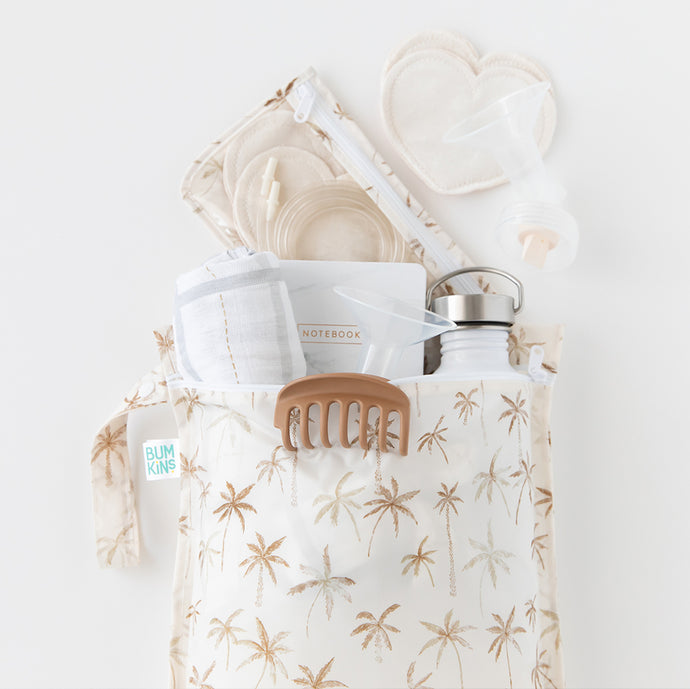 A beige bag with tan palm tree pattern on a white background with a water bottle, cloth, notebook, & breast pump parts peeking out of the top.